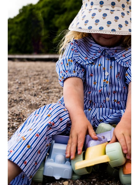 Person i stribet blå skjorte og prikket hat med pastelfarvet legetøj på sandunderlag.